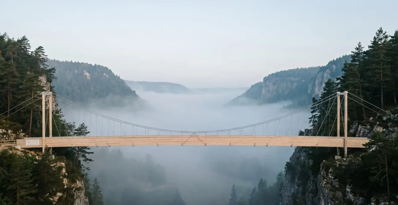 Pont suspendu moderne en bois et acier traversant une vallée brumeuse, symbolisant une migration Cloud progressive et sécurisée entre deux environnements